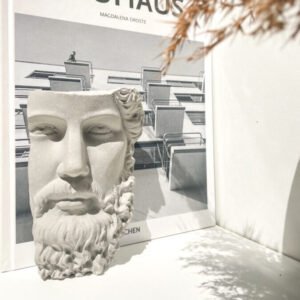 Sculpture visage de dieu grec en béton utilisée comme serre-livres design.